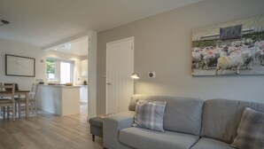A living room with a grey sofa, a small table, and a painting of sheep.