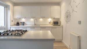 A modern kitchen with white cabinets, a gas stove, a microwave, and a sink.