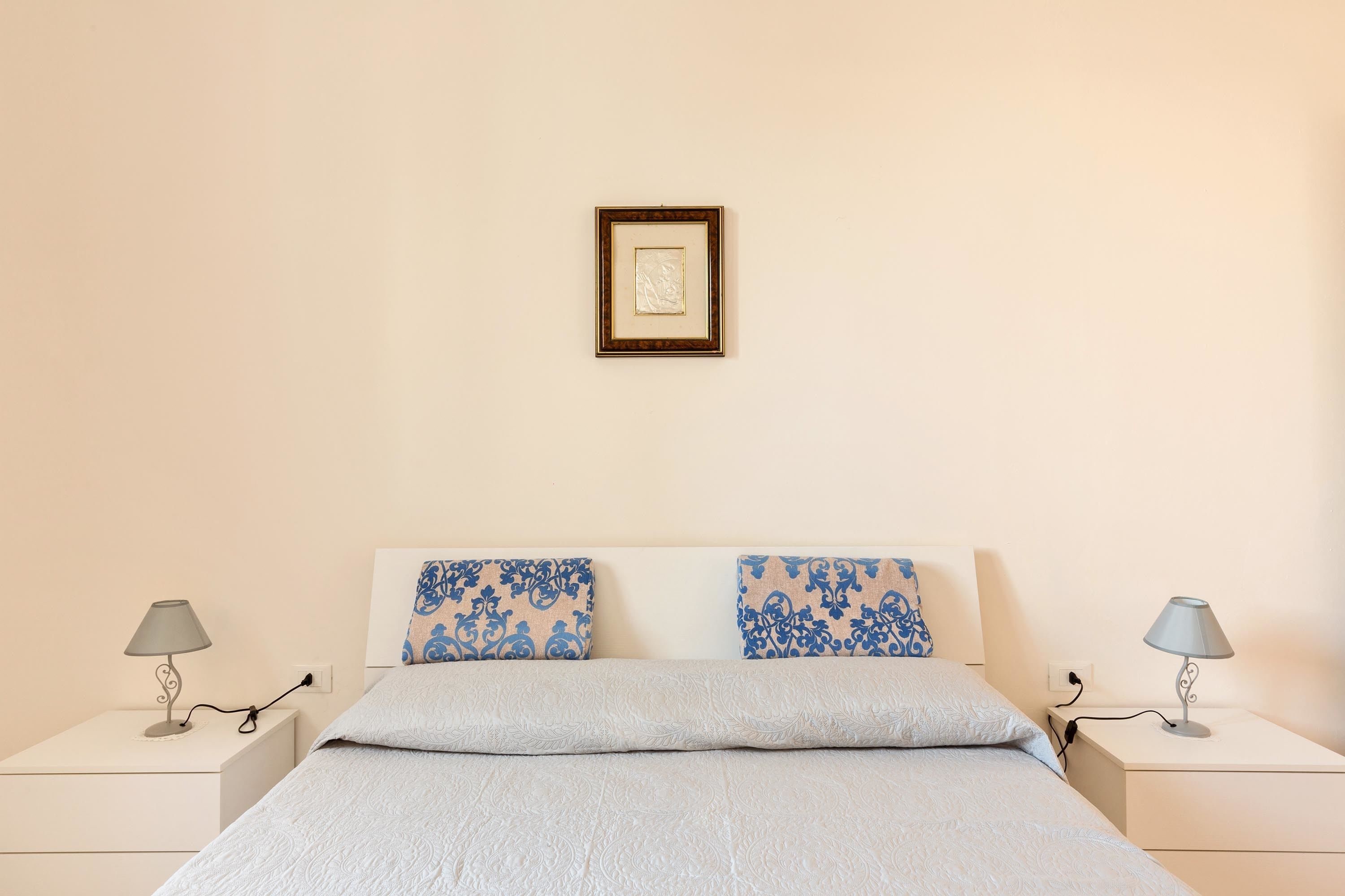 A neatly made bed with a light blue bedspread, two pillows with blue floral patterns, and two bedside tables with lamps.