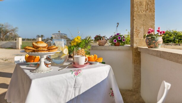 A table set with pastries, a cup, and a vase of flowers on an outdoor patio with a clear view of the sky. - Villetta Evelyn (Montesano Salentino)