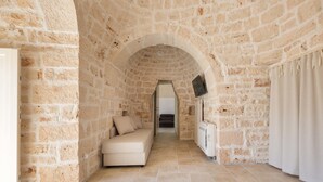 A stone-walled room with a sofa, a flat-screen TV, and a radiator. - Trulli di Buontempo (Francavilla Fontana)