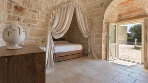 A bedroom with a stone wall, a bed with a wooden headboard, and a view of the outside. - Trulli di Buontempo (Francavilla Fontana)