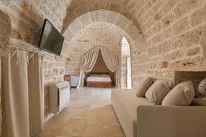 A room with a stone wall, a bed with a canopy, a TV mounted on the wall, and a sofa. - Trulli di Buontempo (Francavilla Fontana)
