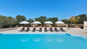 A swimming pool with lounge chairs and umbrellas, surrounded by trees and stone walls. - Trulli di Buontempo (Francavilla Fontana)