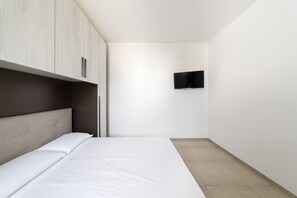 A minimalist bedroom with a bed, a TV mounted on the wall, and a wardrobe. - Quintino Apartments (Nardò)