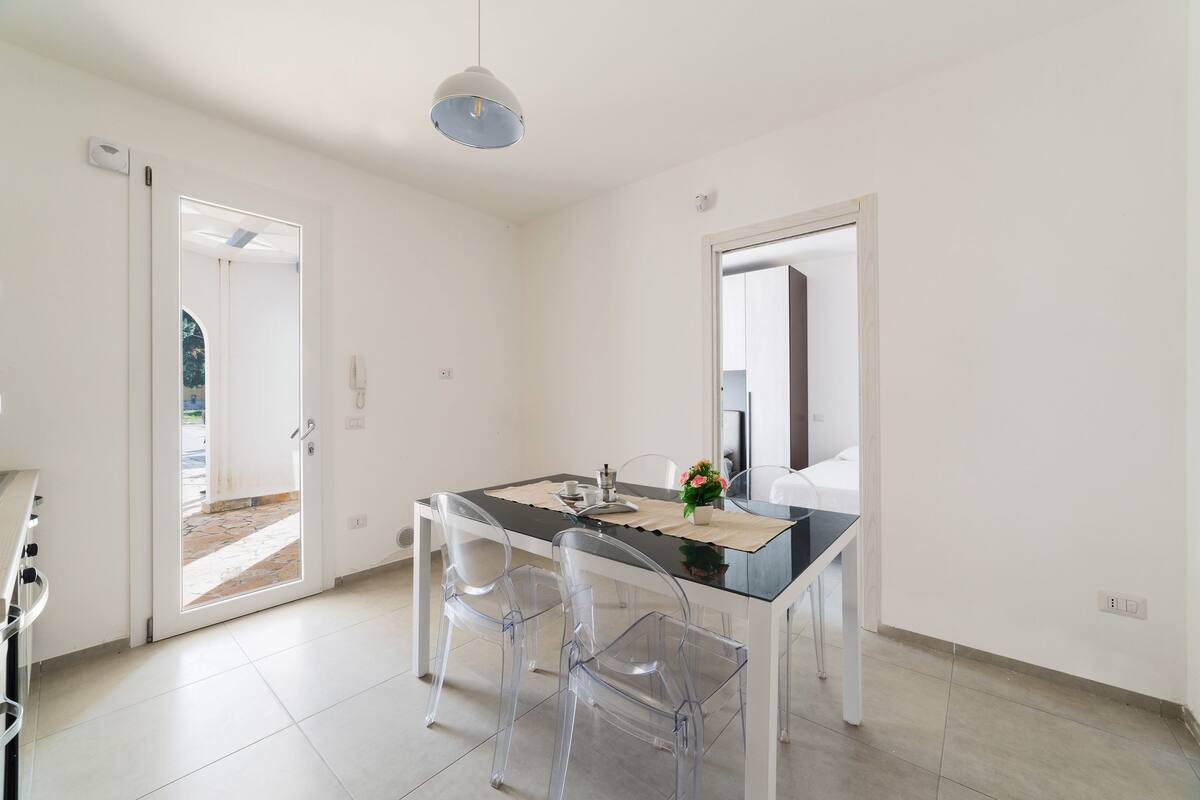 Uma cozinha moderna com bancada branca, cadeiras transparentes e luminária pendente.
