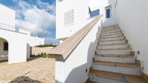 Ein weißes Gebäude mit einem gepflasterten Innenhof und einer Treppe, die zu einer zweiten Etage führt.