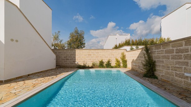 Ein rechteckiger Pool mit klarem, blauem Wasser, umgeben von Steinmauern und weißen Gebäuden.