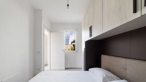 Ein modernes Schlafzimmer mit einem großen Bett, einer Kopfteil und Blick durch eine Tür nach draußen.