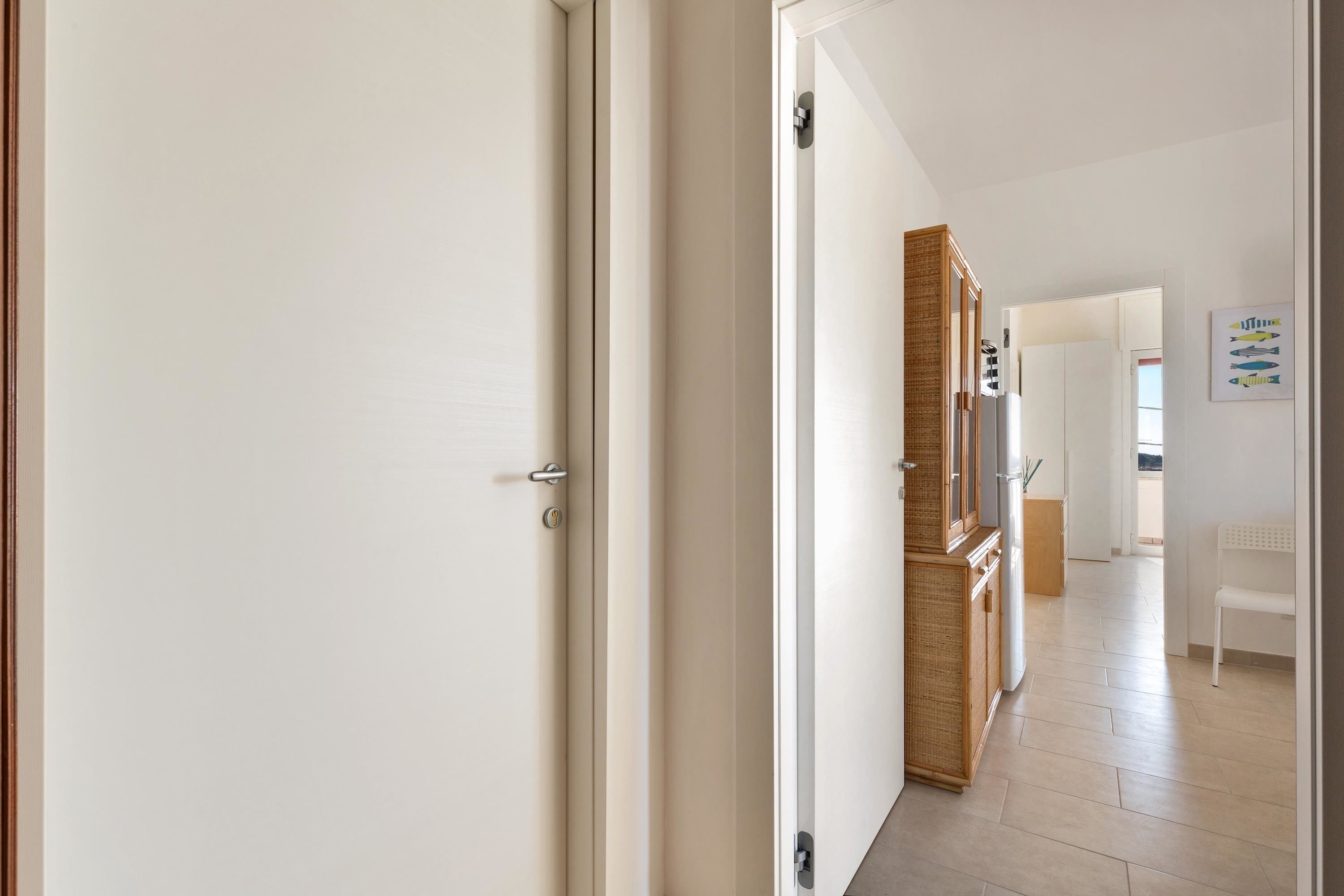Un pasillo con una puerta blanca, un armario de madera y una silla blanca.