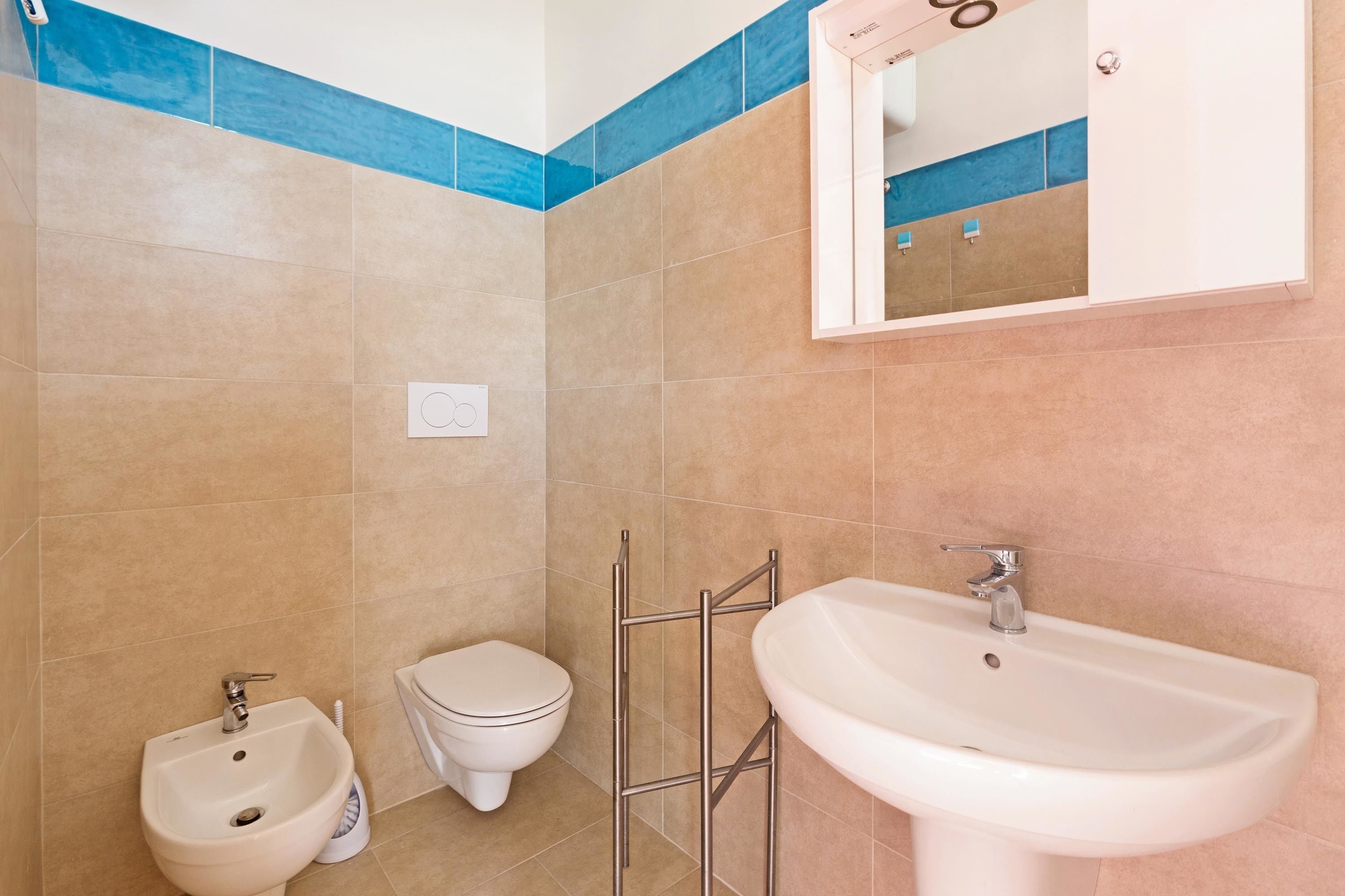 Een badkamer met beige tegels, een witte wastafel, een toiletbrons en een toilet.