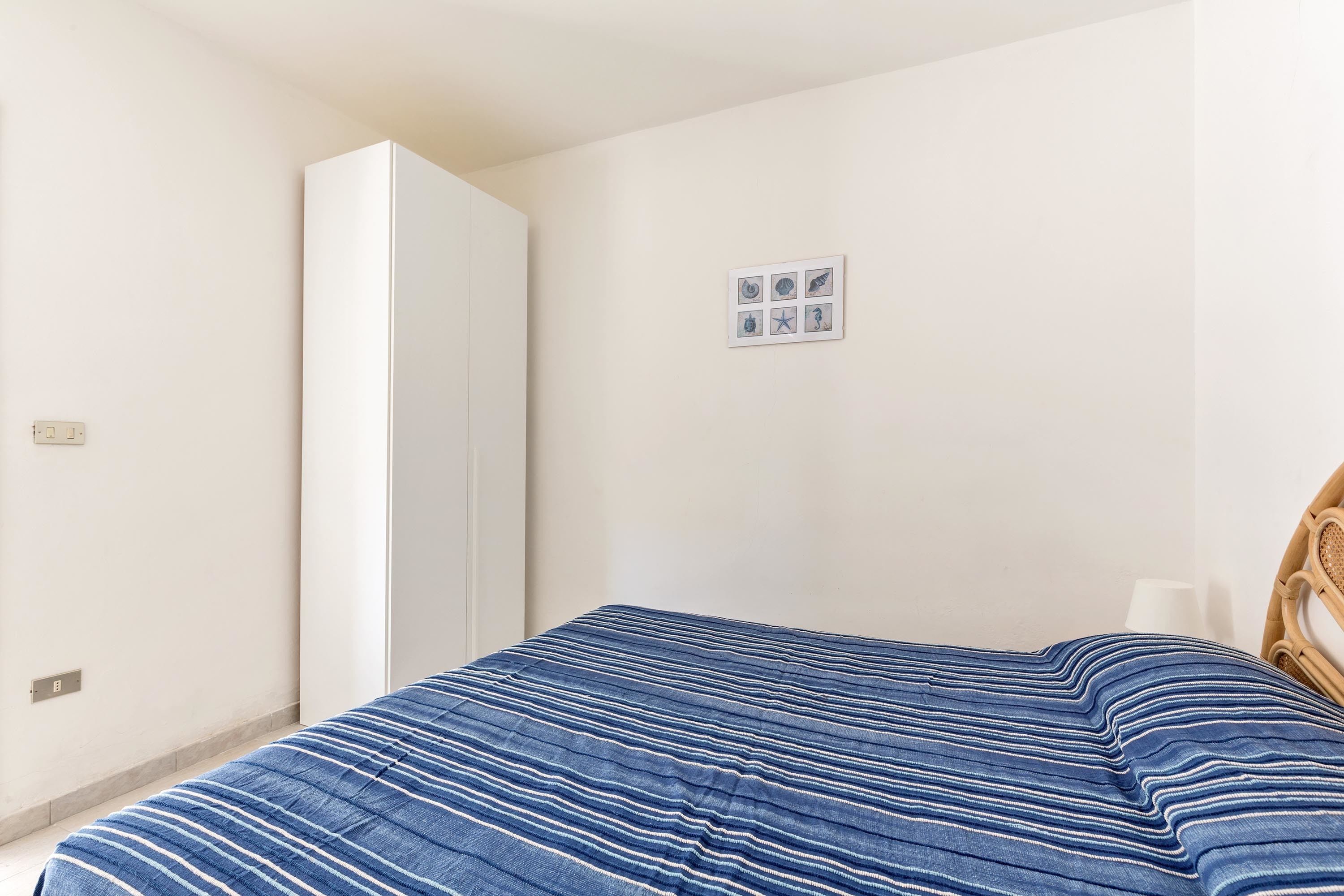 A bedroom with a bed, a wardrobe, and a small wall-mounted picture.