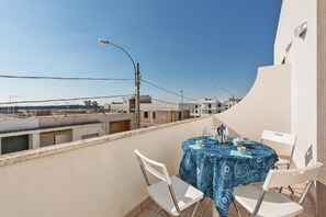 A rooftop terrace with a table and chairs, overlooking a residential area.