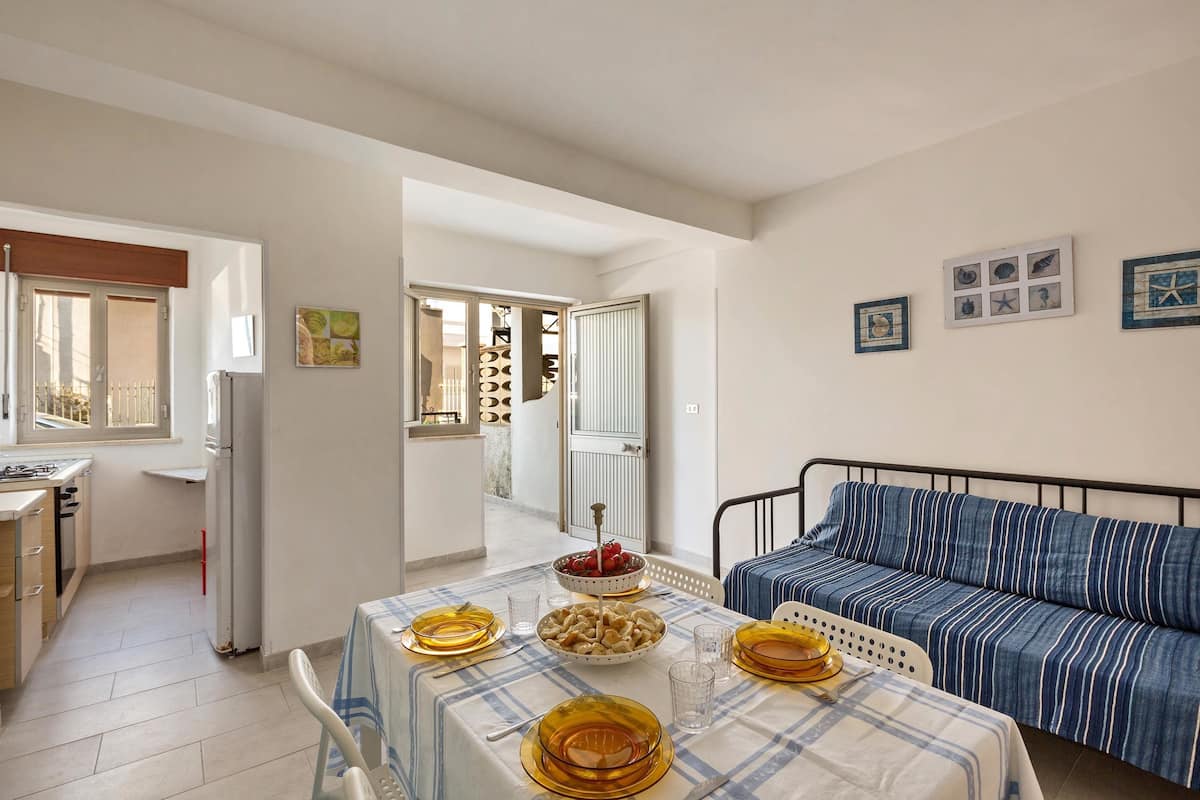 Un coin repas avec une table dressée pour quatre personnes, un canapé et une cuisine en arrière-plan.