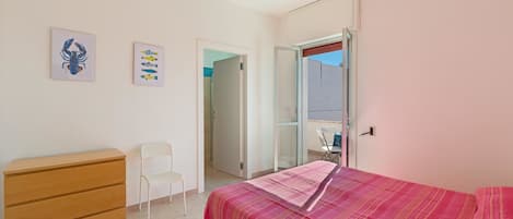 Un dormitorio con una cama, un aparador de madera, una silla blanca y dos cuadros colgados.