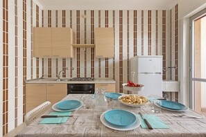 A compact kitchen with striped wallpaper, wooden cabinets, a gas stove, and a white refrigerator.
