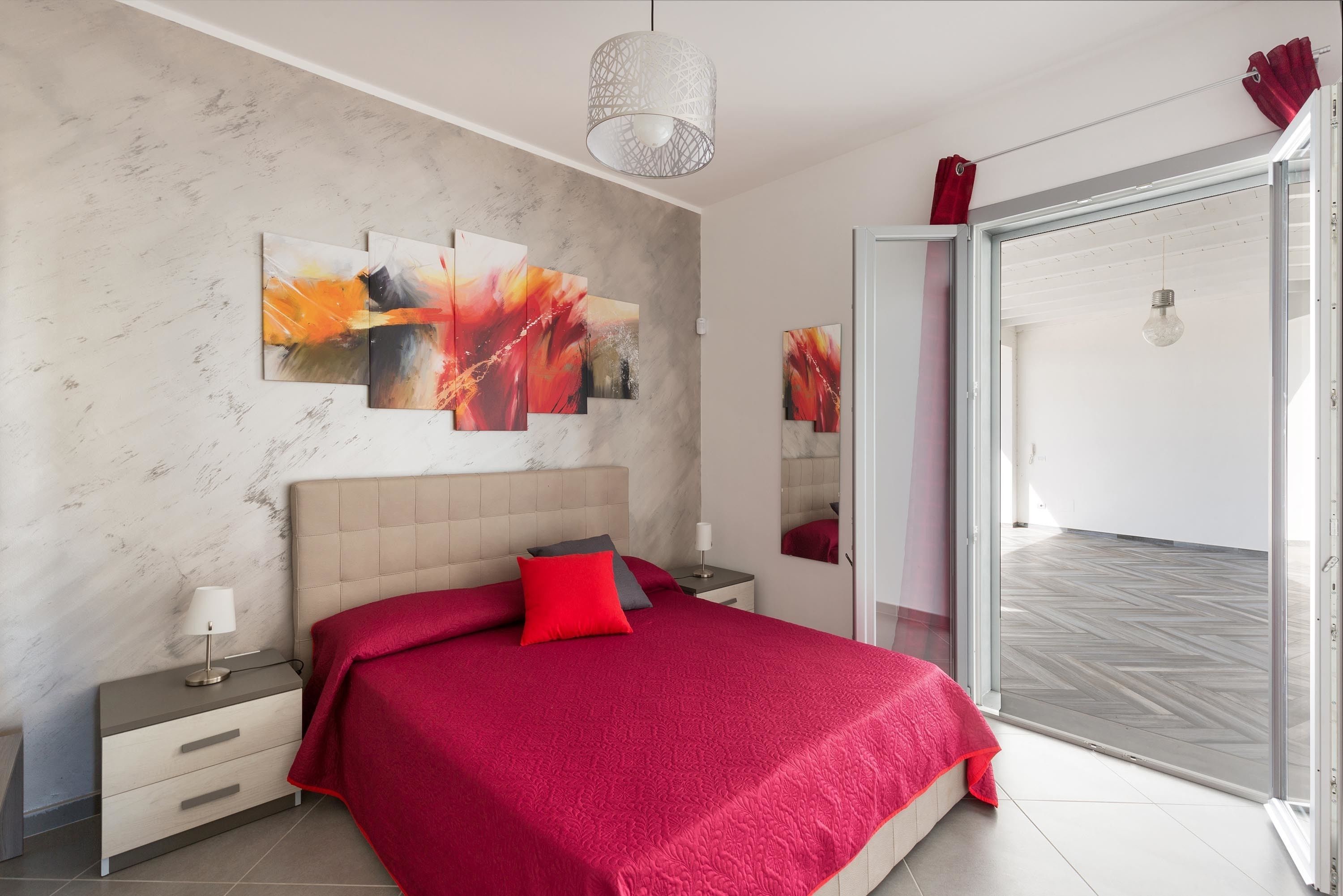 Een moderne slaapkamer met een groot bed, een nachtkastje, een bijzettafeltje en een schuifdeur naar een balkon.