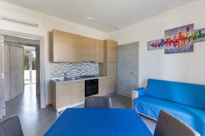 A modern kitchen with wooden cabinets, a tiled backsplash, and a blue sofa in the living area.