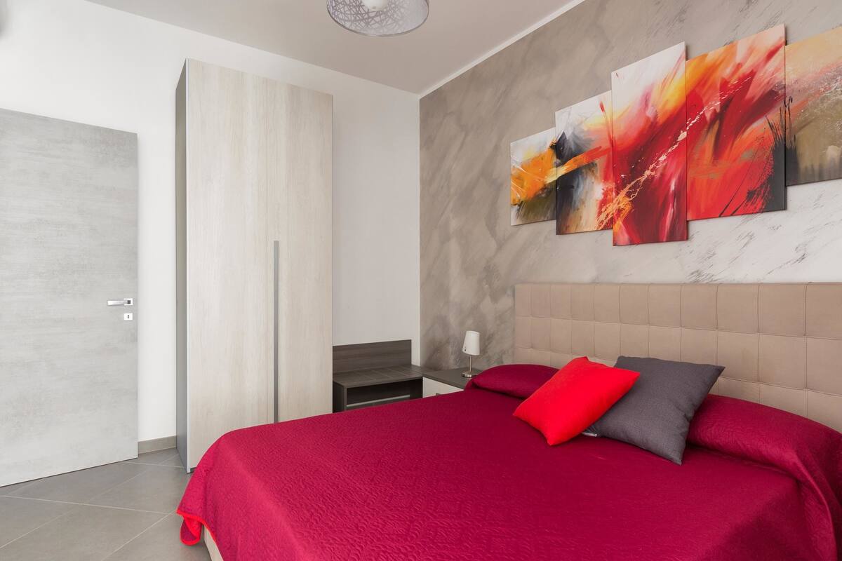 Une chambre moderne avec un grand lit, une armoire et des œuvres d’art abstraites accrochées au mur.