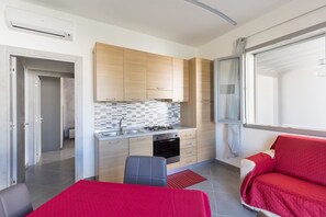 A compact kitchen with wooden cabinets, a tiled backsplash, and a red sofa.