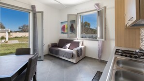 A modern kitchen with a gas stove, a dining table with chairs, a sofa, and large windows offering a view of the outdoors.