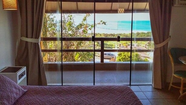 A bedroom with a large window, a bed, a chair, and a small table. - Pousada Bangalôs Da Mole - Florianópolis (Florianópolis)