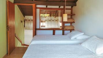 Una habitación con cama, vigas de madera, una ventana con cortinas y una puerta.