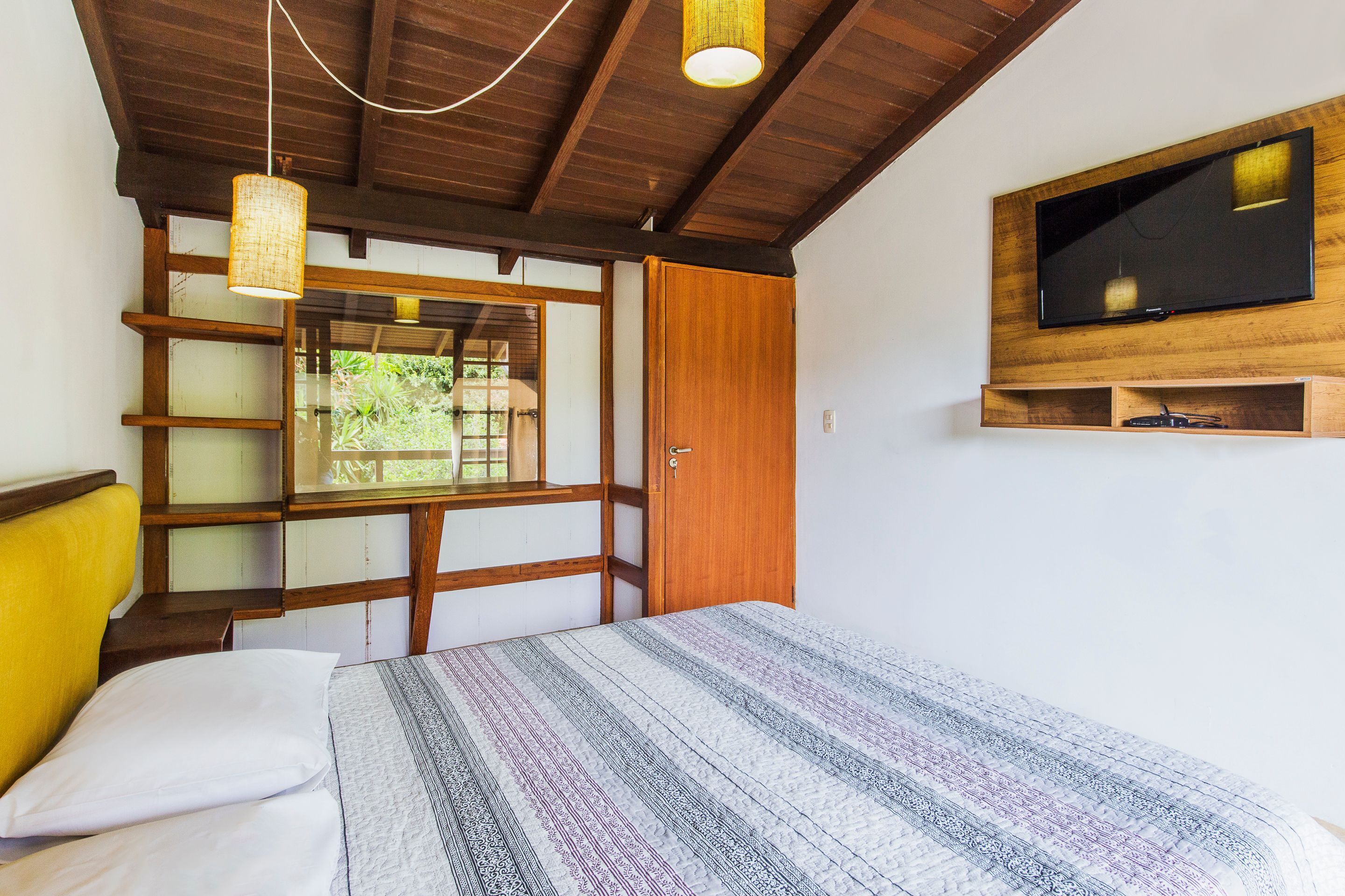 Una habitación con una cama, un televisor montado en la pared y un ventanal con vistas a zonas verdes.