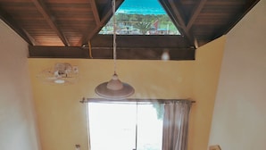 A room with a sloped ceiling, a large window with curtains, and a hanging light fixture. - Pousada Bangalôs Da Mole - Florianópolis (Florianópolis)