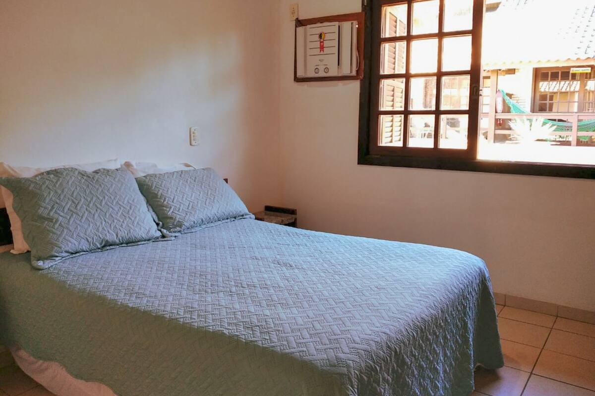 A bedroom with a bed, pillows, a thermostat, and a window with a view of the outside.
