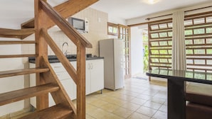 A kitchen with wooden beams, a refrigerator, a microwave, and a window with a view of greenery. - Pousada Bangalôs Da Mole - Florianópolis (Florianópolis)
