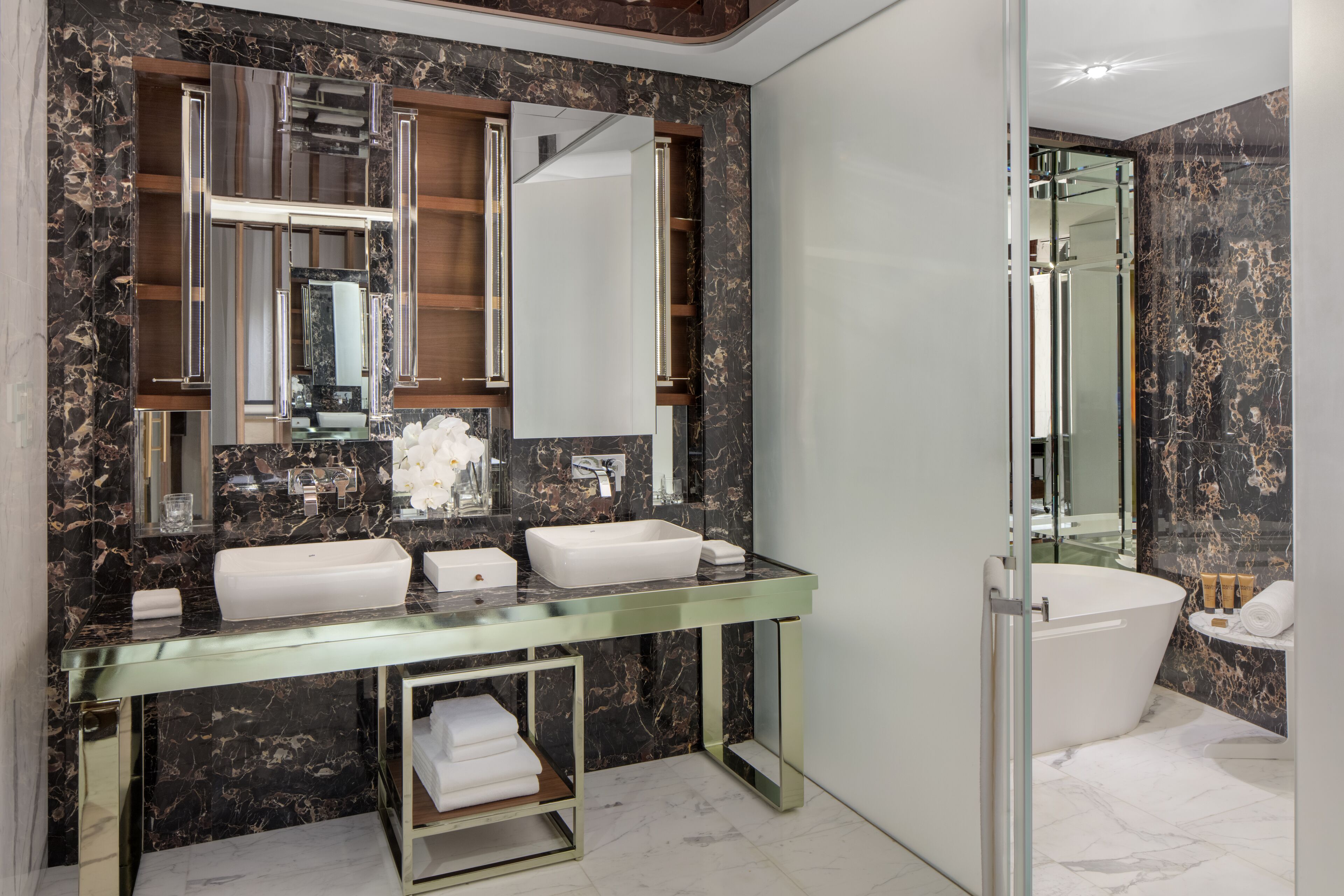 A modern bathroom with a glass vanity, two sinks, a large mirror, and a separate shower area.
