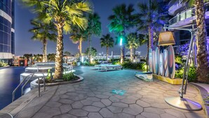 A nighttime outdoor area with palm trees, a pool, and a modern building with glass balconies. - Paramount Hotel Dubai (Dubai)