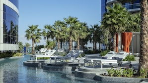 A pool area with lounge chairs, palm trees, and a modern building in the background. - Paramount Hotel Dubai (Dubai)