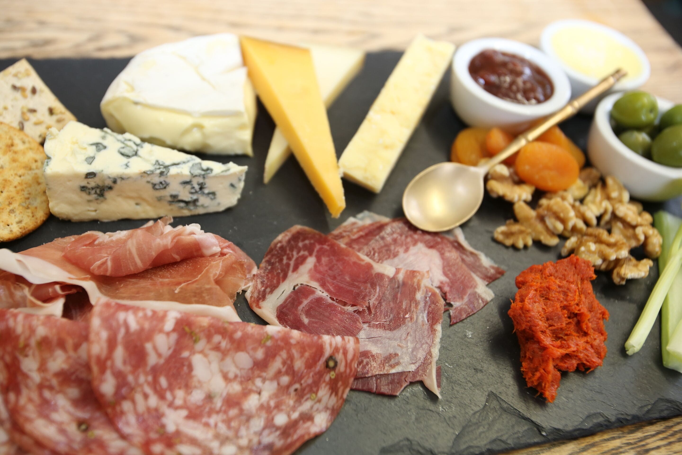 A variety of cheeses, meats, and nuts on a slate board.