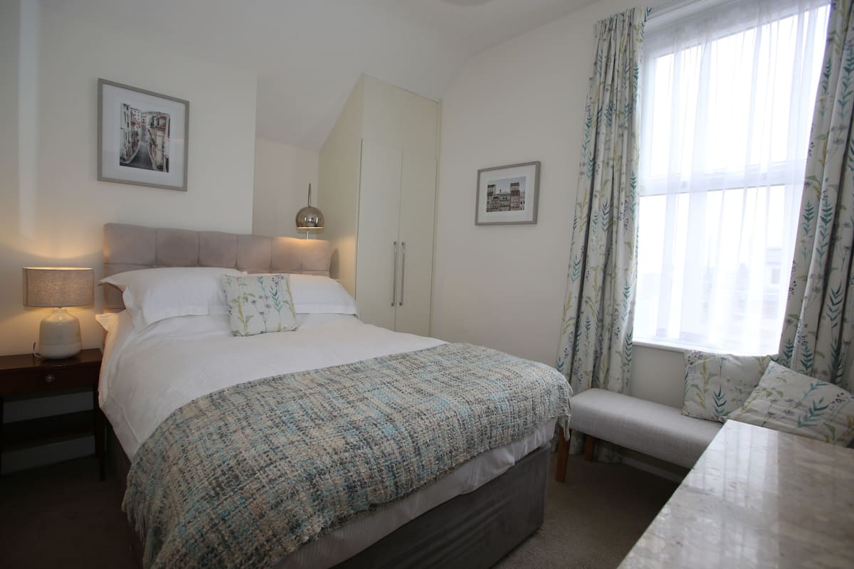 A bedroom with a bed, bedside tables, a bench, a wardrobe, and two framed pictures on the wall.