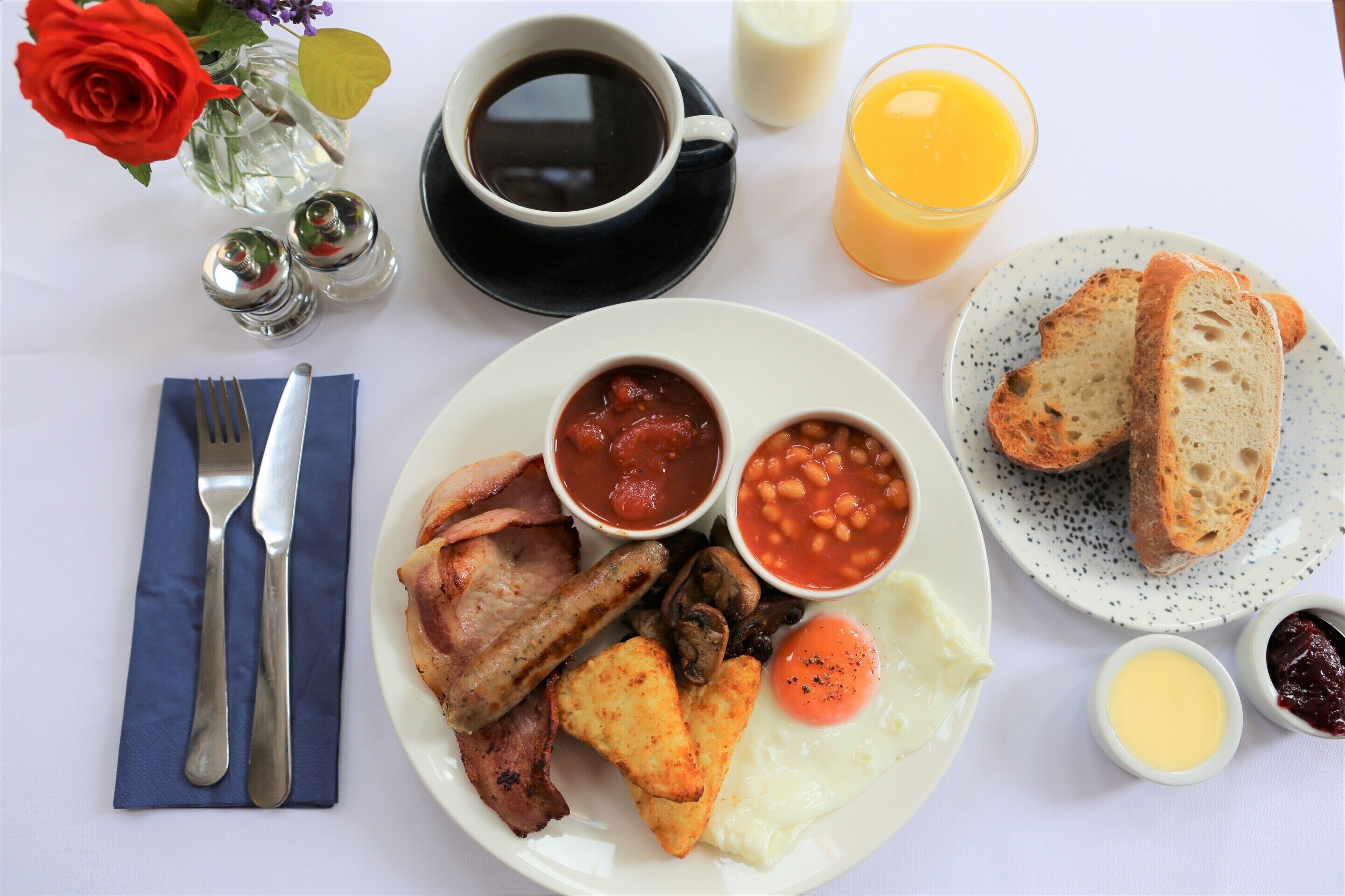 A breakfast plate with bacon, eggs, beans, toast, and a cup of coffee.
