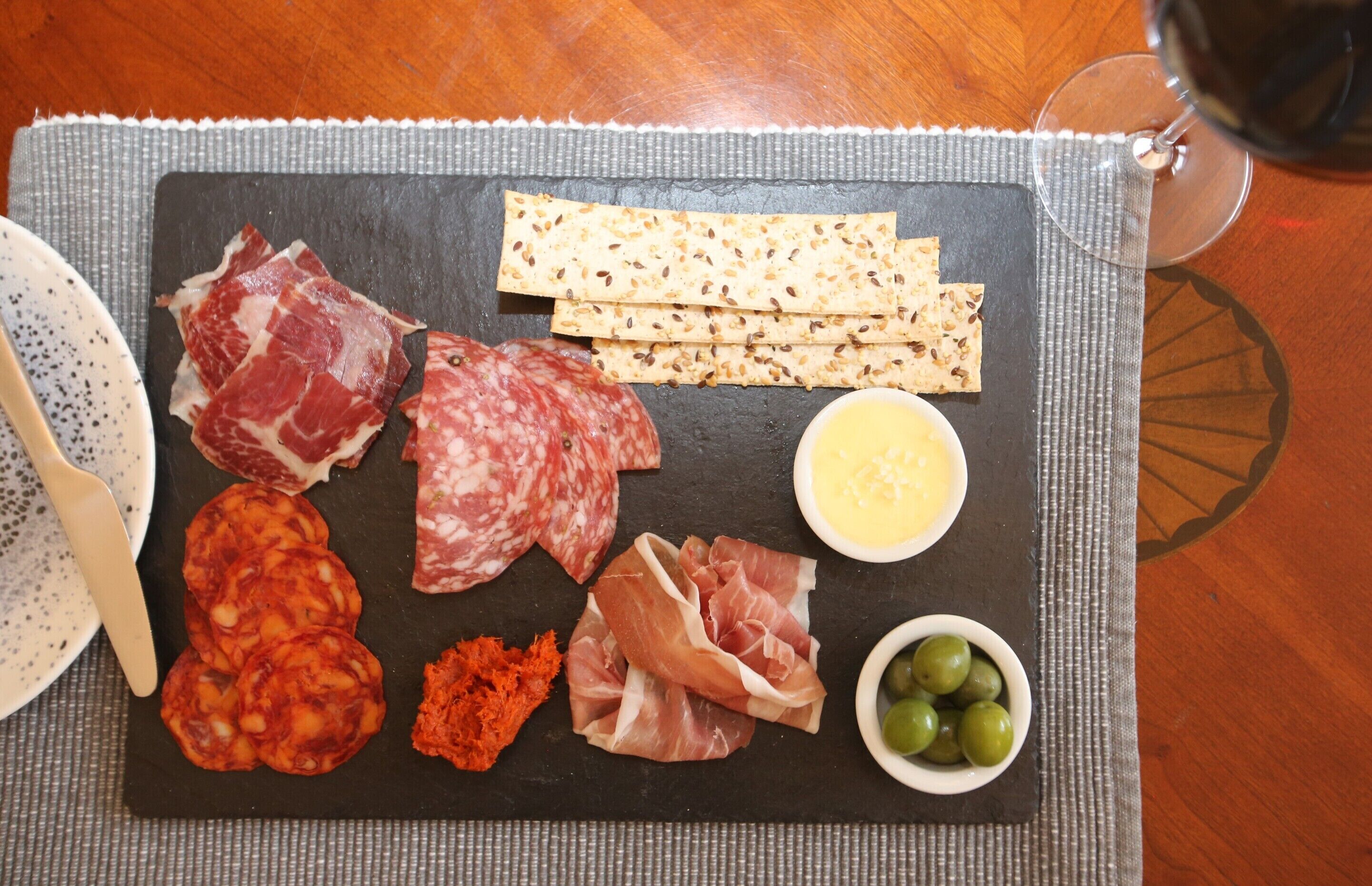 Una tabla de fiambres con diferentes carnes, quesos y aceitunas sobre una tabla de pizarra.