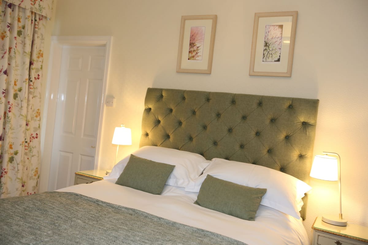 A neatly made bed with a tufted headboard, two bedside lamps, and a floral curtain.