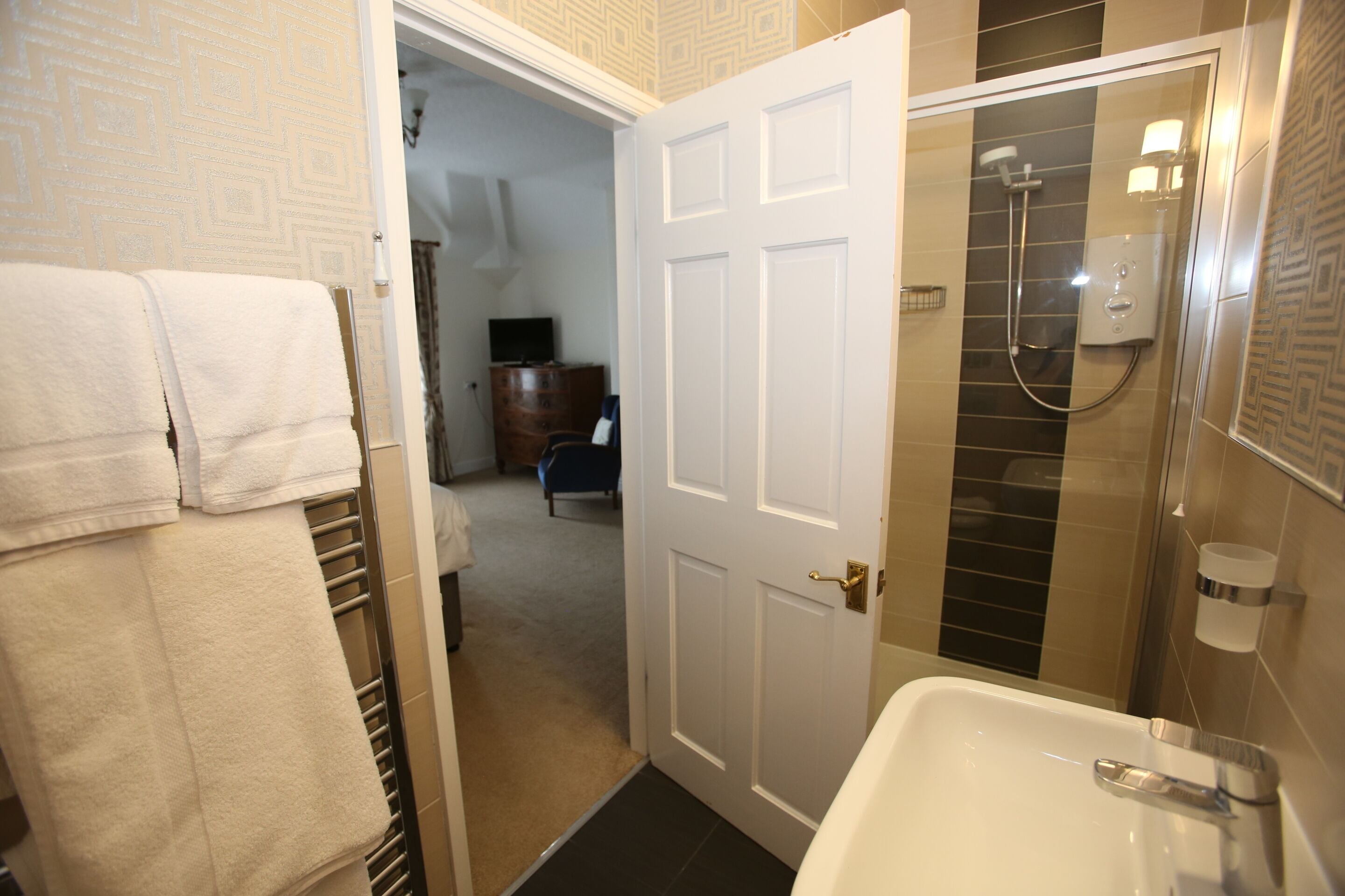 Un baño con un lavabo blanco, una ducha con puerta de cristal y un perchero con toallas dobladas.