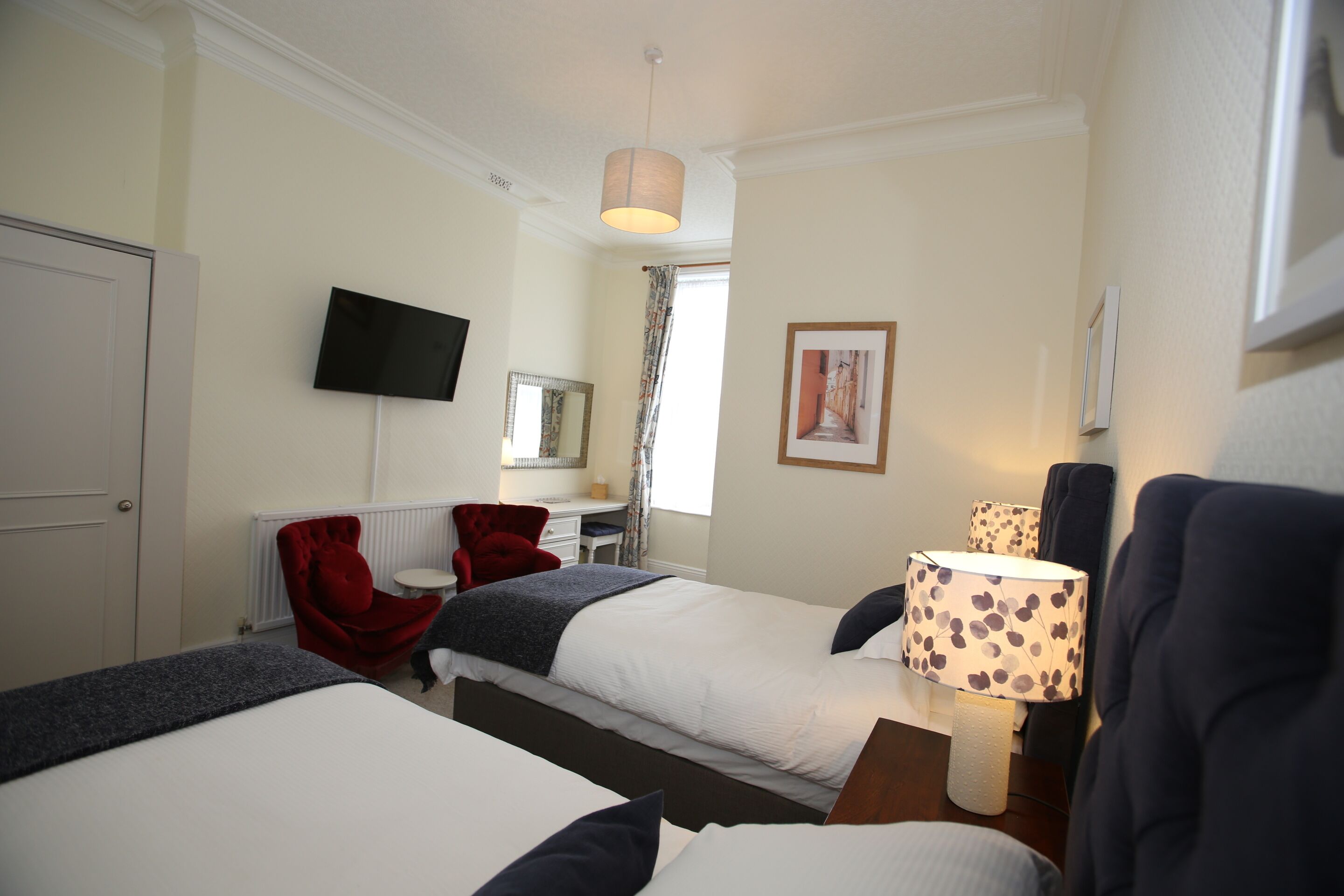 A hotel room with two beds, a desk, a chair, a television, and a window with curtains.