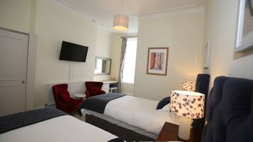 A hotel room with two beds, a desk, a chair, a television, and a window with curtains.