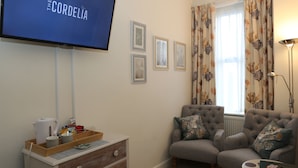 A living room with a television, two armchairs, a coffee table, a sideboard, and framed pictures on the wall. - The Cordelia (Scarborough)