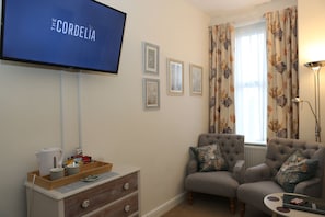 Una sala de estar con televisor, dos sillones, una mesita de centro, un aparador y cuadros enmarcados en la pared.