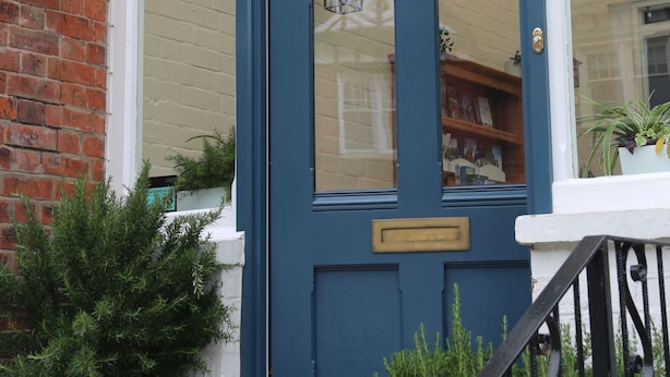 A blue door with a brass handle, a white window above, and a brick wall. - The Cordelia (Scarborough)