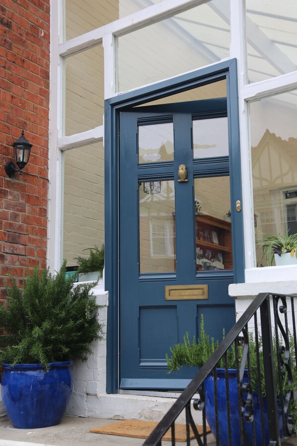 A blue door with a brass handle, a white window above, and a brick wall. - The Cordelia (Scarborough)