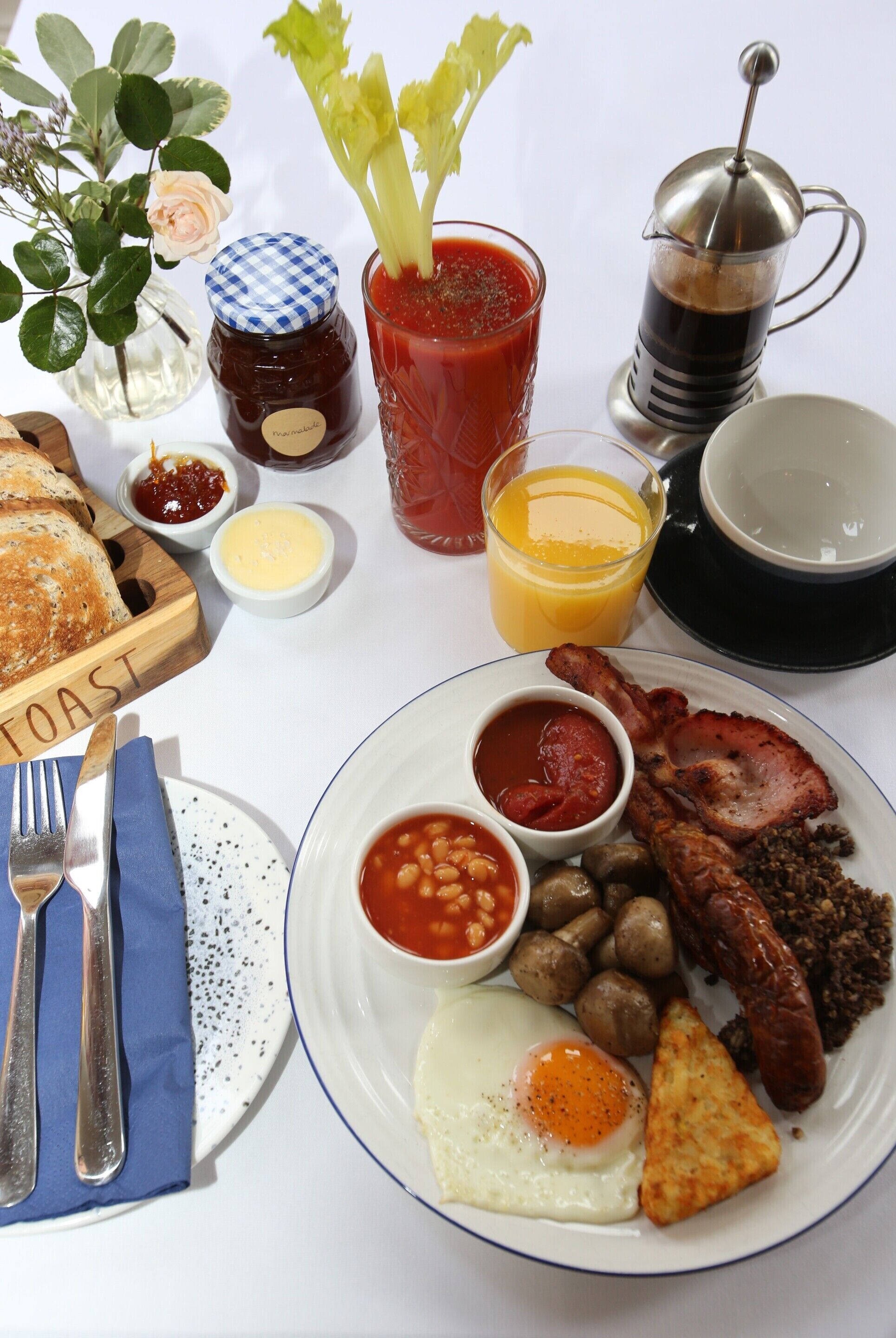 A breakfast plate with eggs, bacon, sausages, beans, mushrooms, toast, and a glass of orange juice.