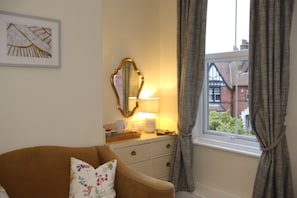 A room with a brown sofa, a mirror, a lamp, a window with curtains, and a framed picture on the wall. - The Cordelia (Scarborough)
