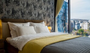 Relax in a spacious room with a large bed, wooden headboard, and city views.