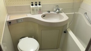 Ein kleines Badezimmer mit Toilette, Waschbecken und Badewanne. Auf der Ablage am Waschbecken stehen drei Toilettenartikel.